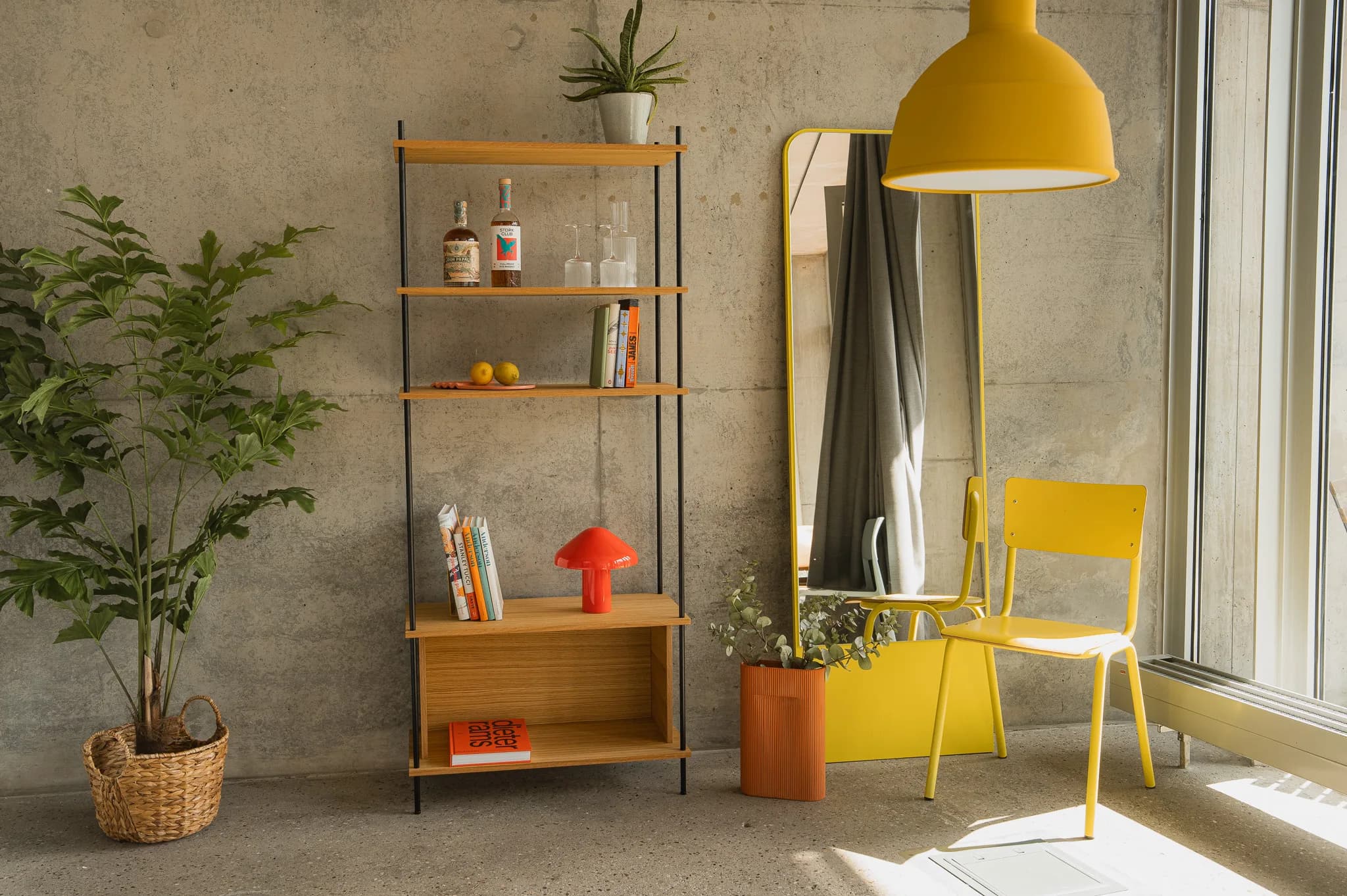 Loft-Wohnzimmer mit KUUDU-Standing-Regal, Pflanze in Topf oben, Whiskeyflasche und Karaffen, roter Mushroom-Lampe, daneben gelber Bistro-Stuhl und Pendelleuchte